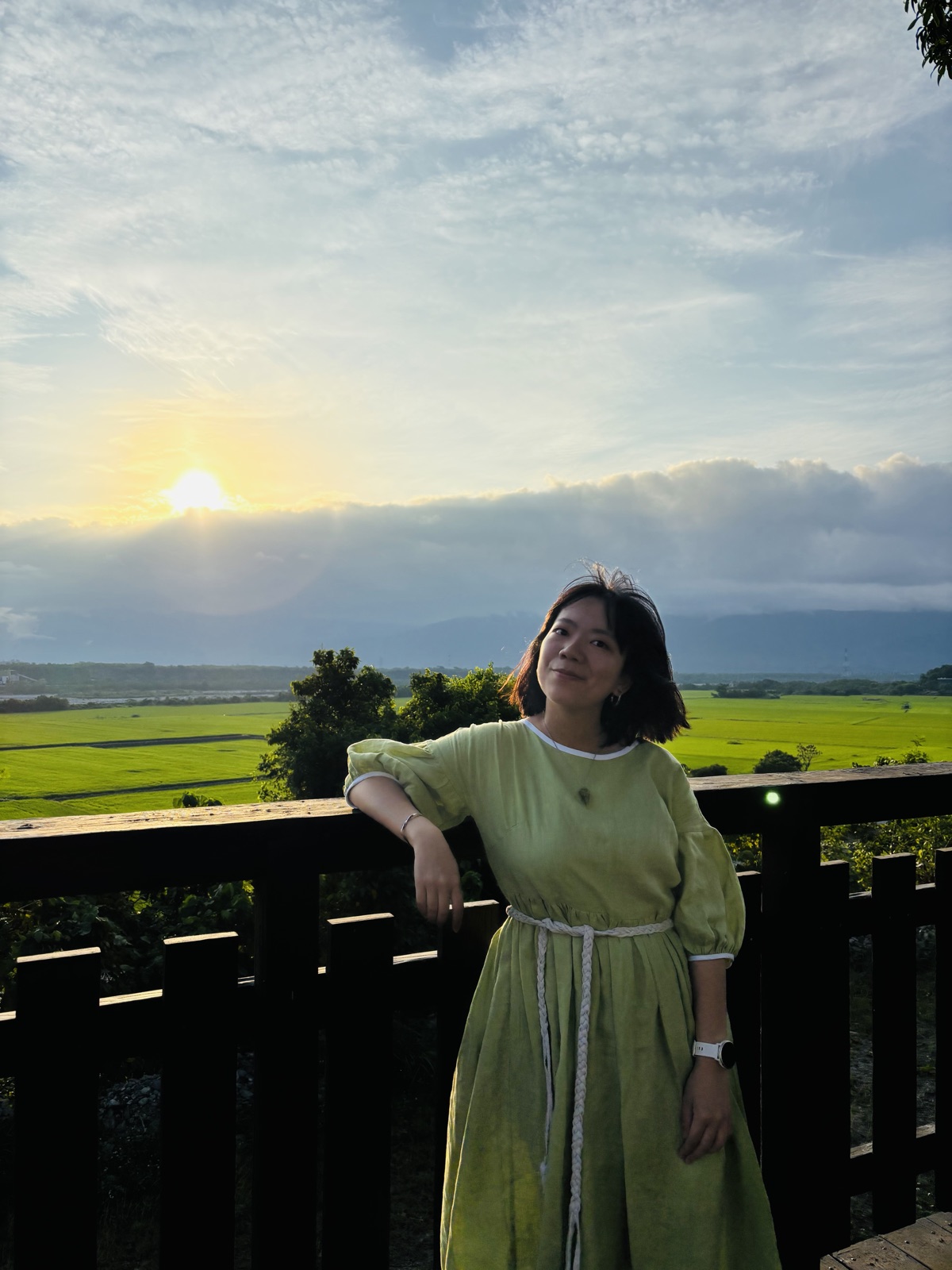 Jasmine 在夕陽下的稻田邊，靠著木欄杆微笑